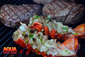 Upside down Lobster tails and steaks being grilled
