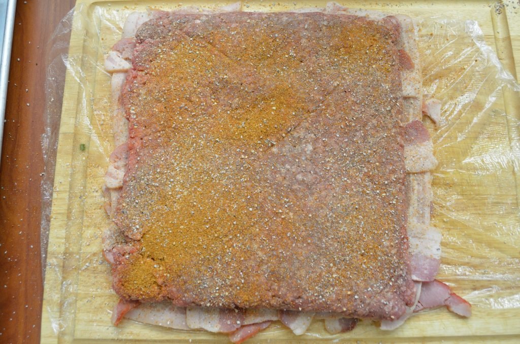 Next, stuff a plastic freezer bag with about 2lbs of ground chuck and evenly flatten the bag. Tear open the bag and lay the beef on the bacon. Season with your favorite BBQ rub - here with used a combination of SuckleBusters SPG and Competition Rubs.