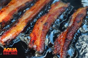 Four slices of bacon being fried in grease